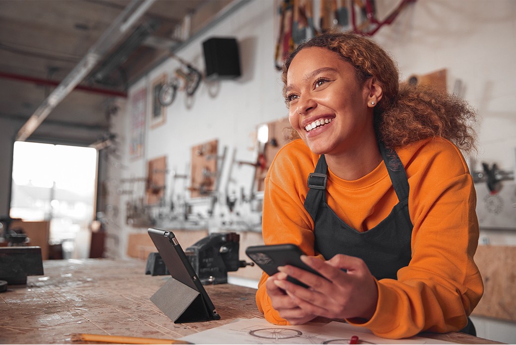 Profissional autônoma sorrindo enquanto usa o celular em sua oficina